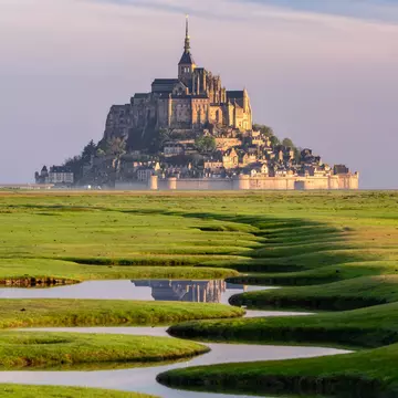 A river curves through green grass with a cathedral on a hill at the end.