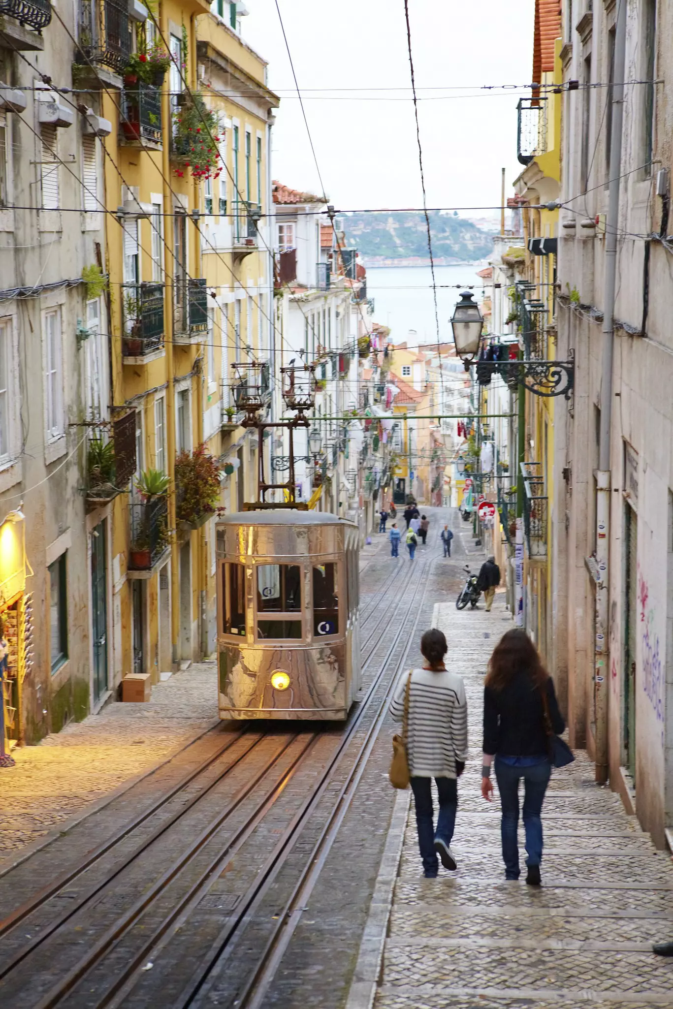 People walking past a funicular tram on a cobbled street in Lisbon, Portugal.