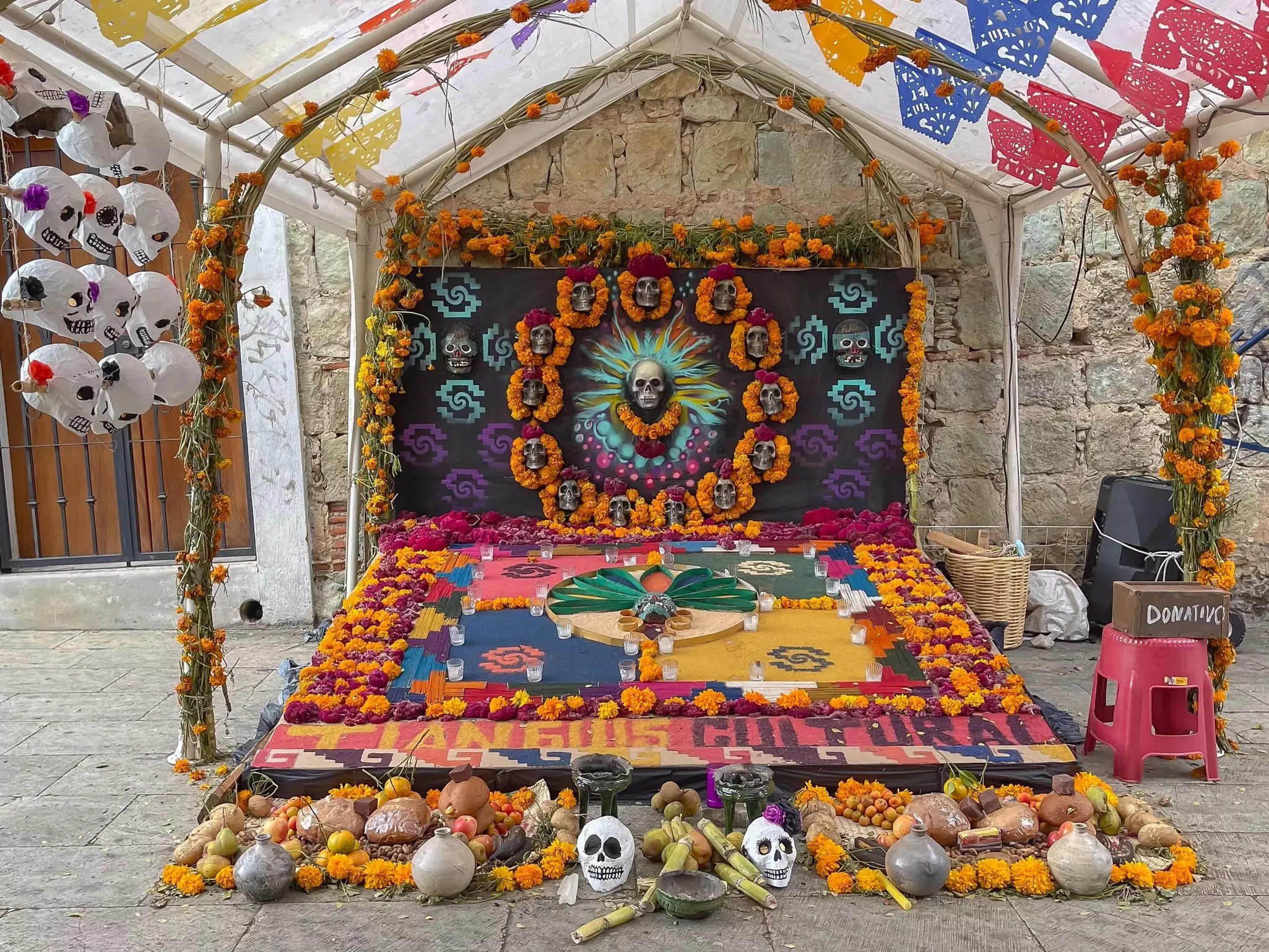 Day of the Dead offerings, including papier mache skulls and marigolds, fashioned into art on a city street.