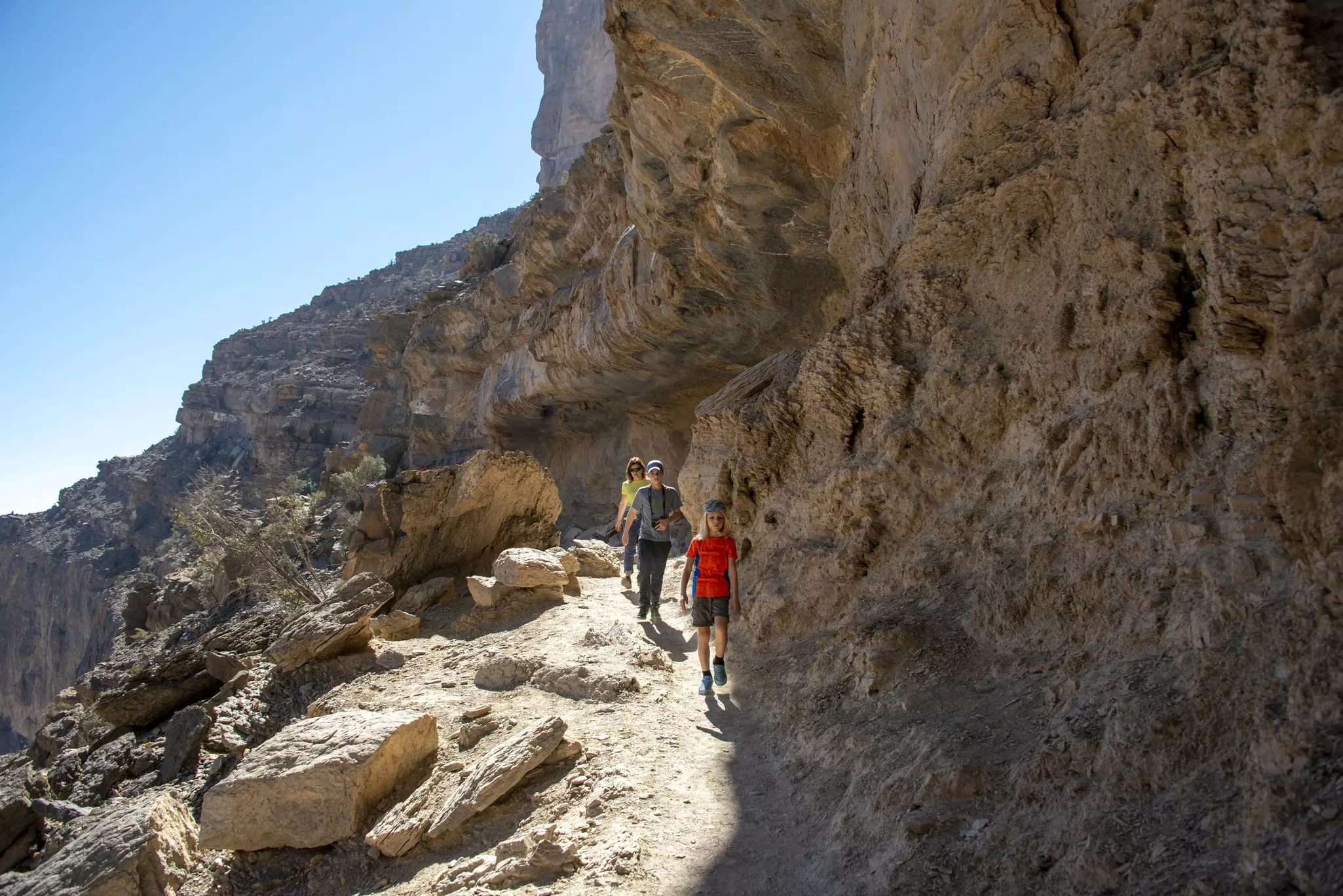 A family group hiking along a rocky path on the edge of a canyon