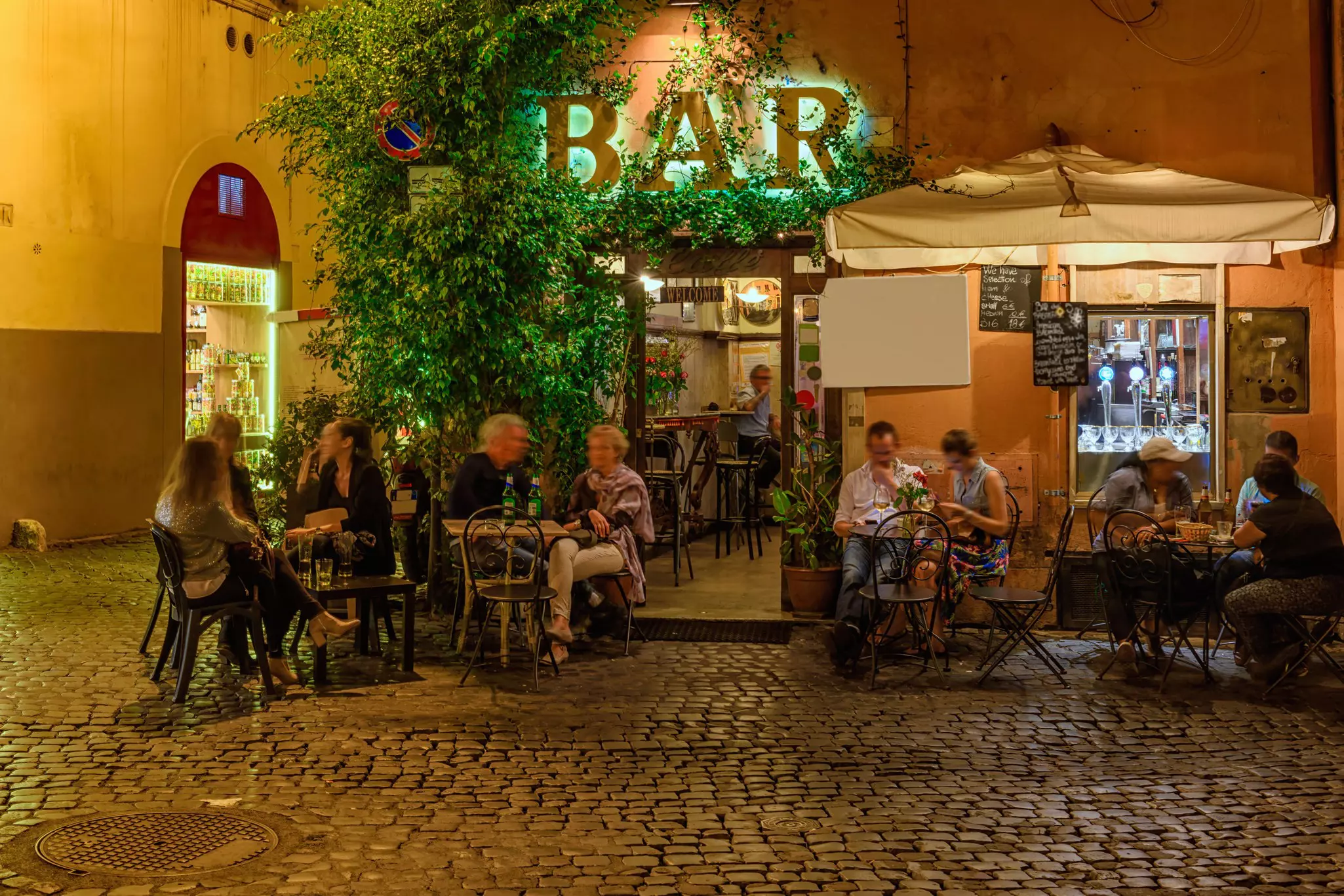 People sit outside a bar on an old street at night in Trastevere