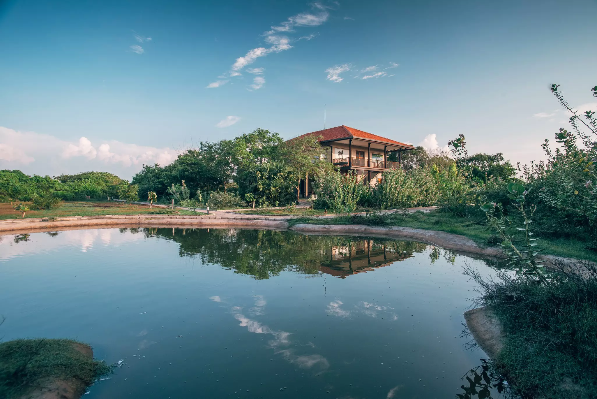The red roof of a lodge house near a large pond peeks out above the surrounding trees and bushes