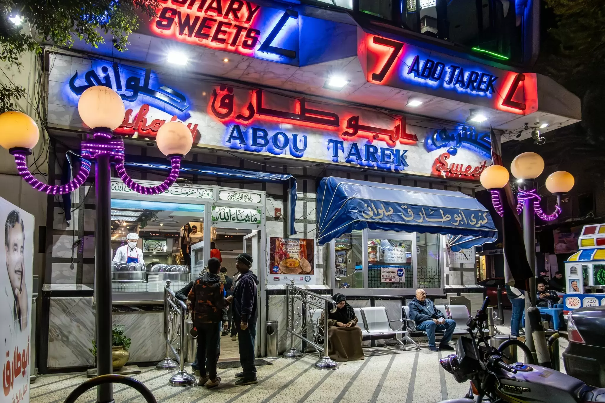 People outside a restaurant with blue and red neon signs at night