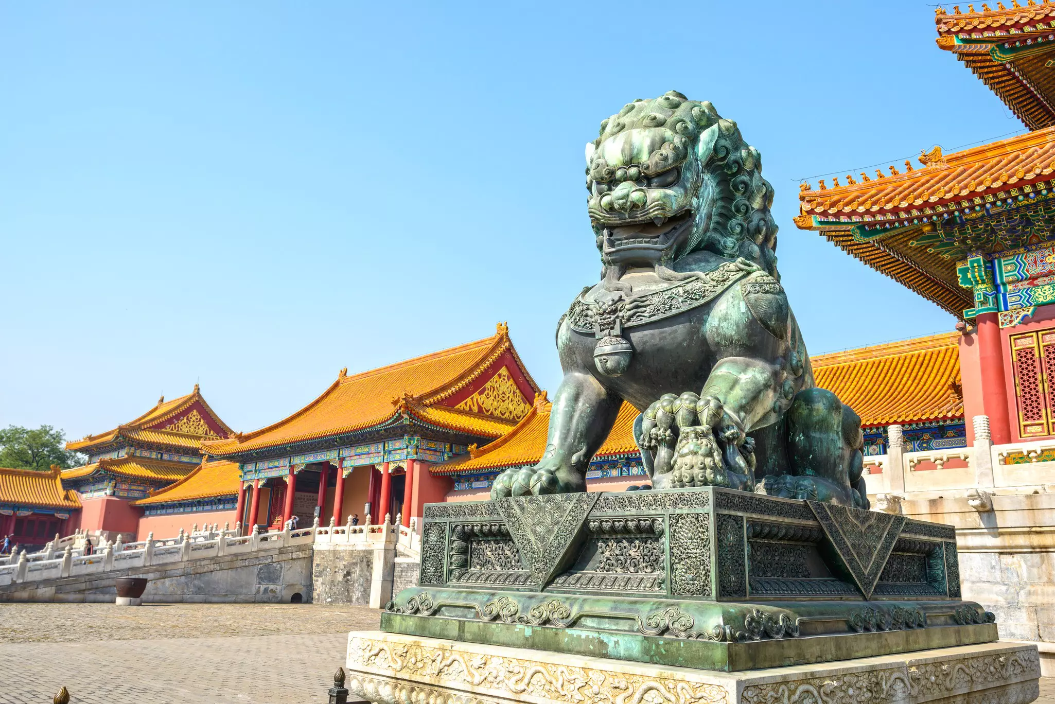 Bronze Chinese guardian lion with yellow-roofed buildings in the background.