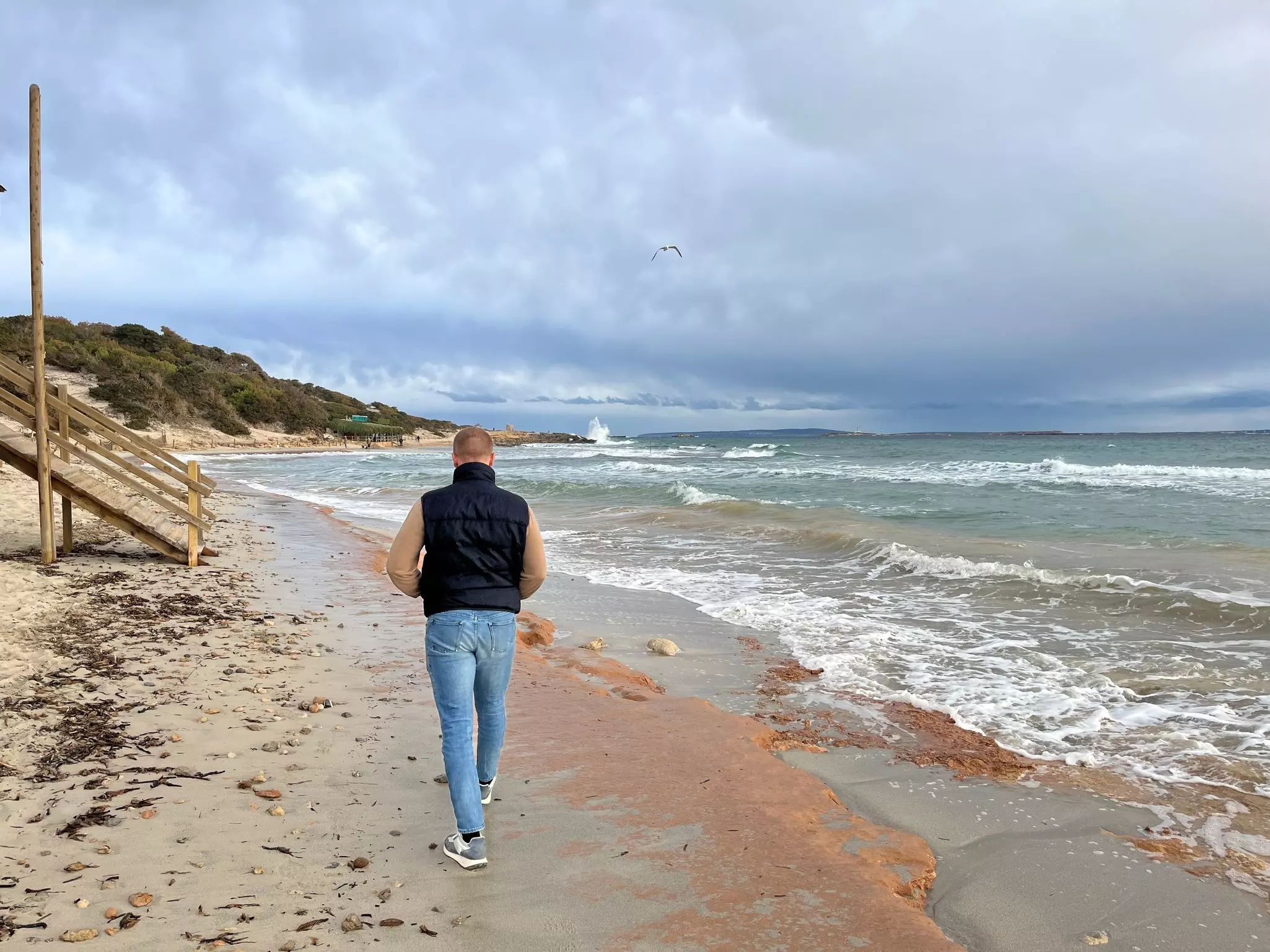 A man is seen from behind walking on a beach in winter.