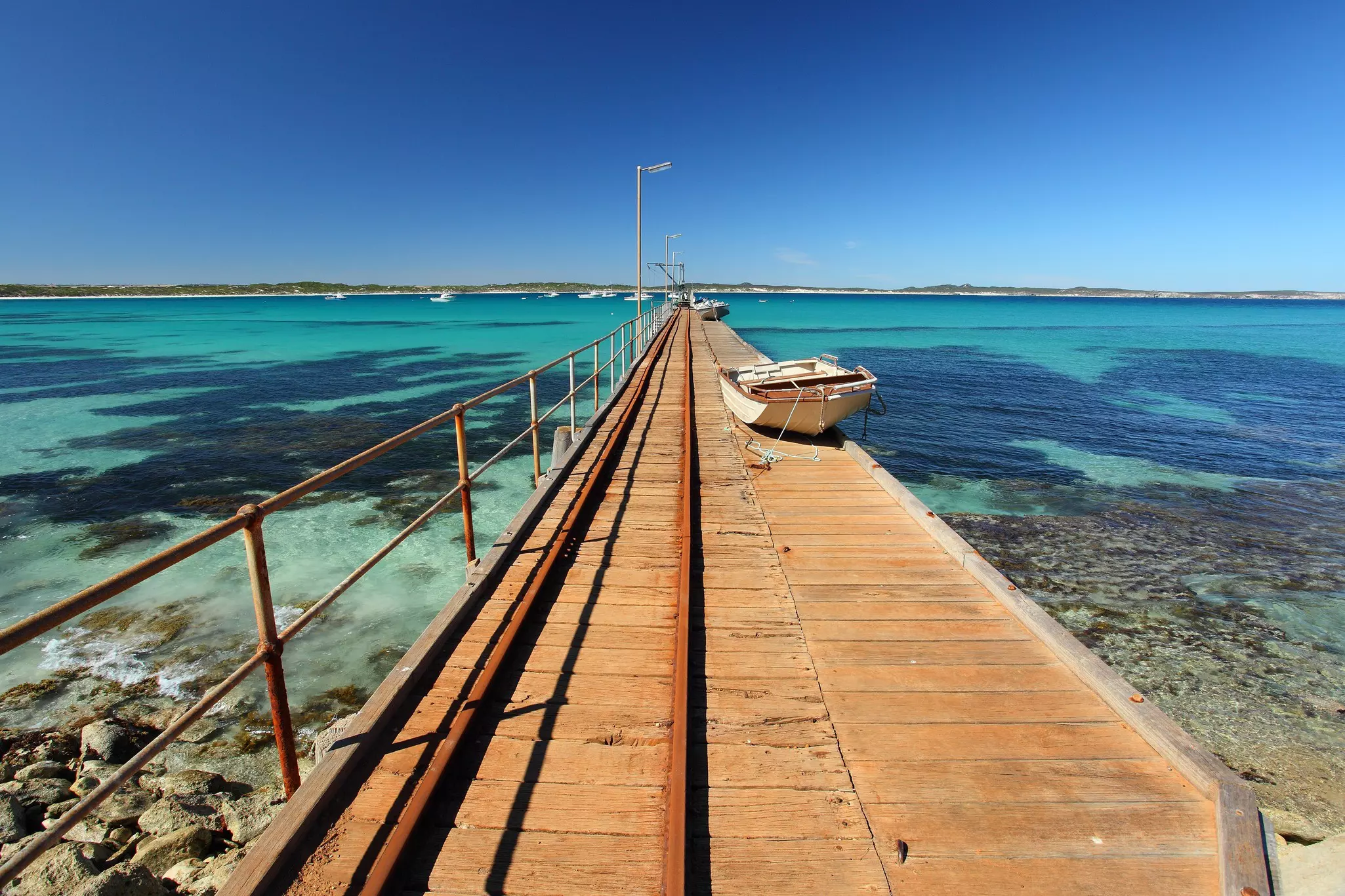 A long wooden jetty, with two small row boats docked on it, stretches out into turquoise ocean.