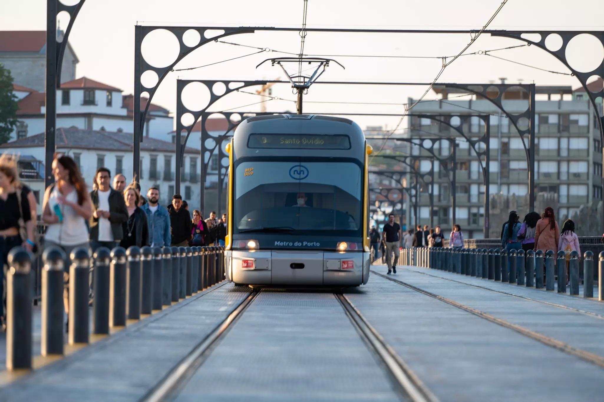 A tram crosses a bridge with people walking on the footways either side of the rails.