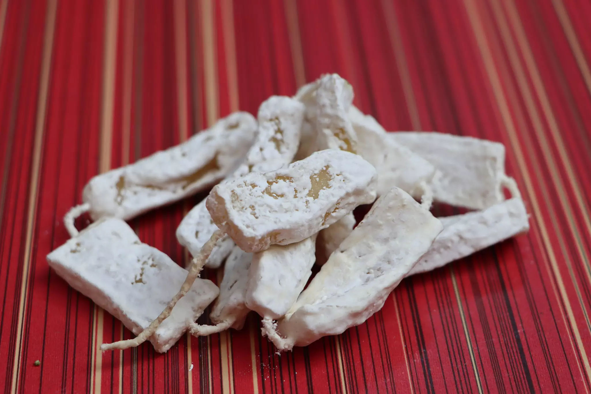 A close up of hard yak cheese (chhurpi) on a string, laid out on a striped red tablecloth