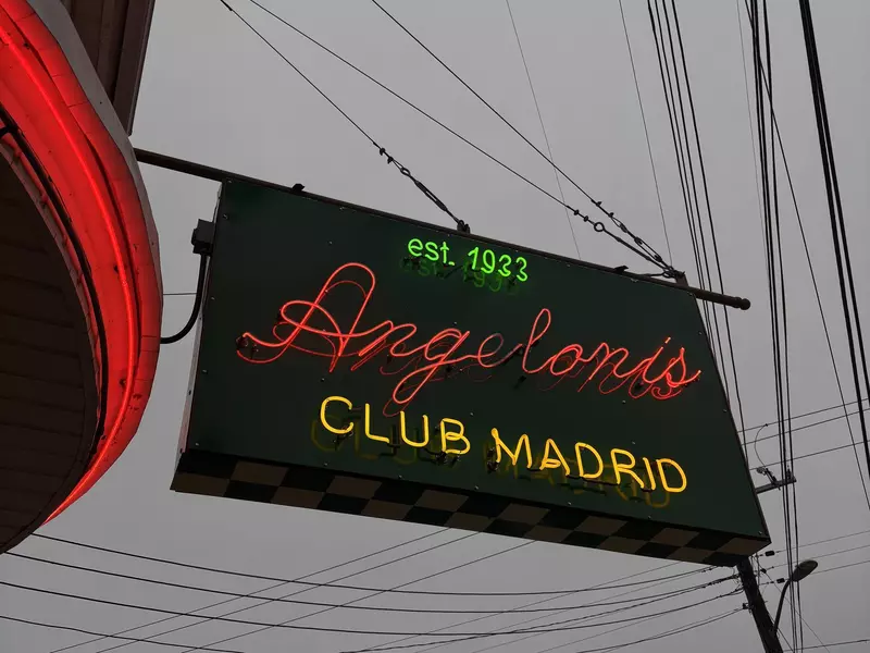 A sign for Angeloni's Club Madrid with green, red and yellow neon letters on a black background