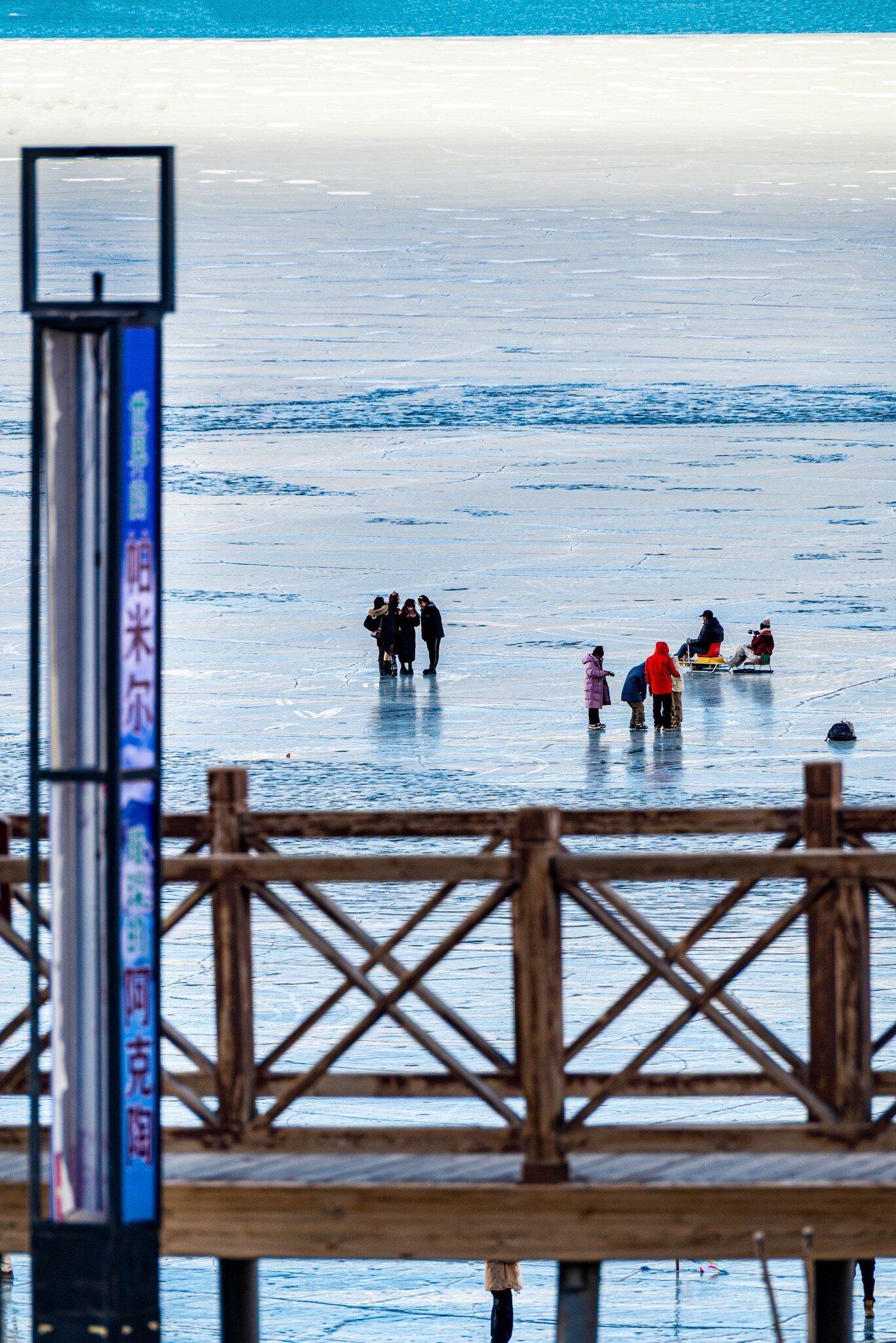 People stand on frozen Baisha Lake behind a wooden railing and a sign reading 帕米尔 and 阿克陶, Xinjiang, China
