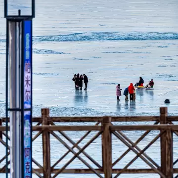 People stand on frozen Baisha Lake behind a wooden railing and a sign reading 帕米尔 and 阿克陶, Xinjiang, China