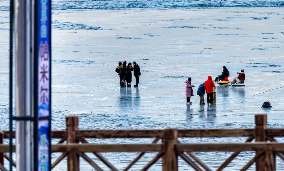People stand on frozen Baisha Lake behind a wooden railing and a sign reading 帕米尔 and 阿克陶, Xinjiang, China