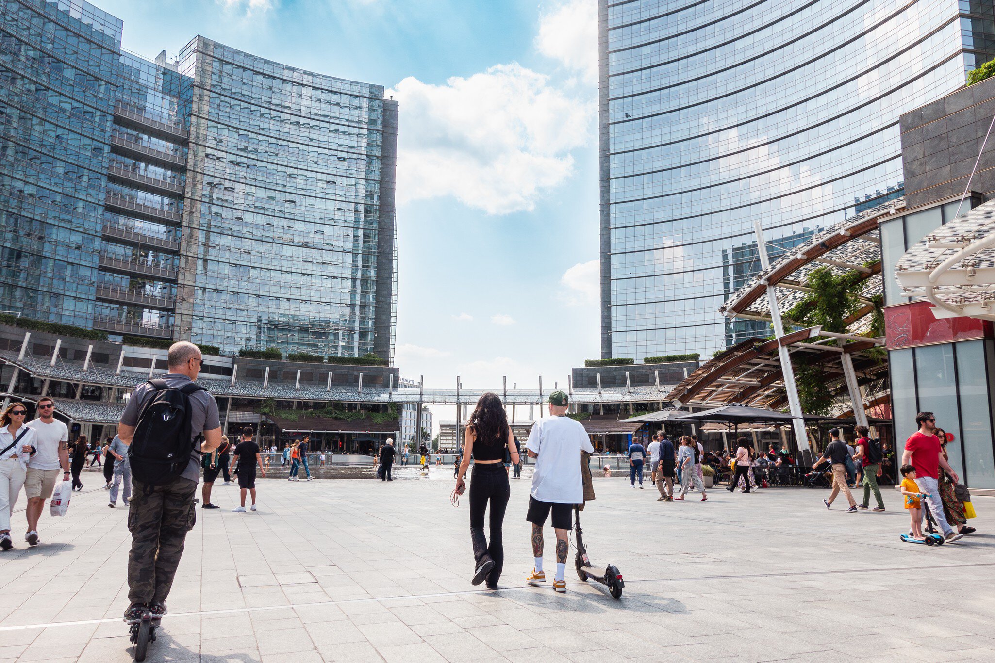 Milan, Gae Aulenti square, people on electric push scooter. Pedestrian zone in modern Milan square with glass buildings and people on electric scooters