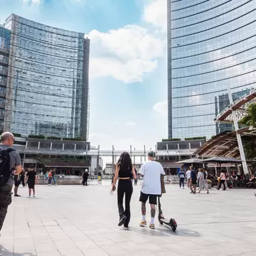 Milan, Gae Aulenti square, people on electric push scooter. Pedestrian zone in modern Milan square with glass buildings and people on electric scooters