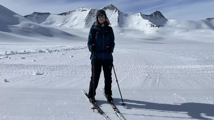 Hikers in deep snow follow a trail downhill through a mountain range.