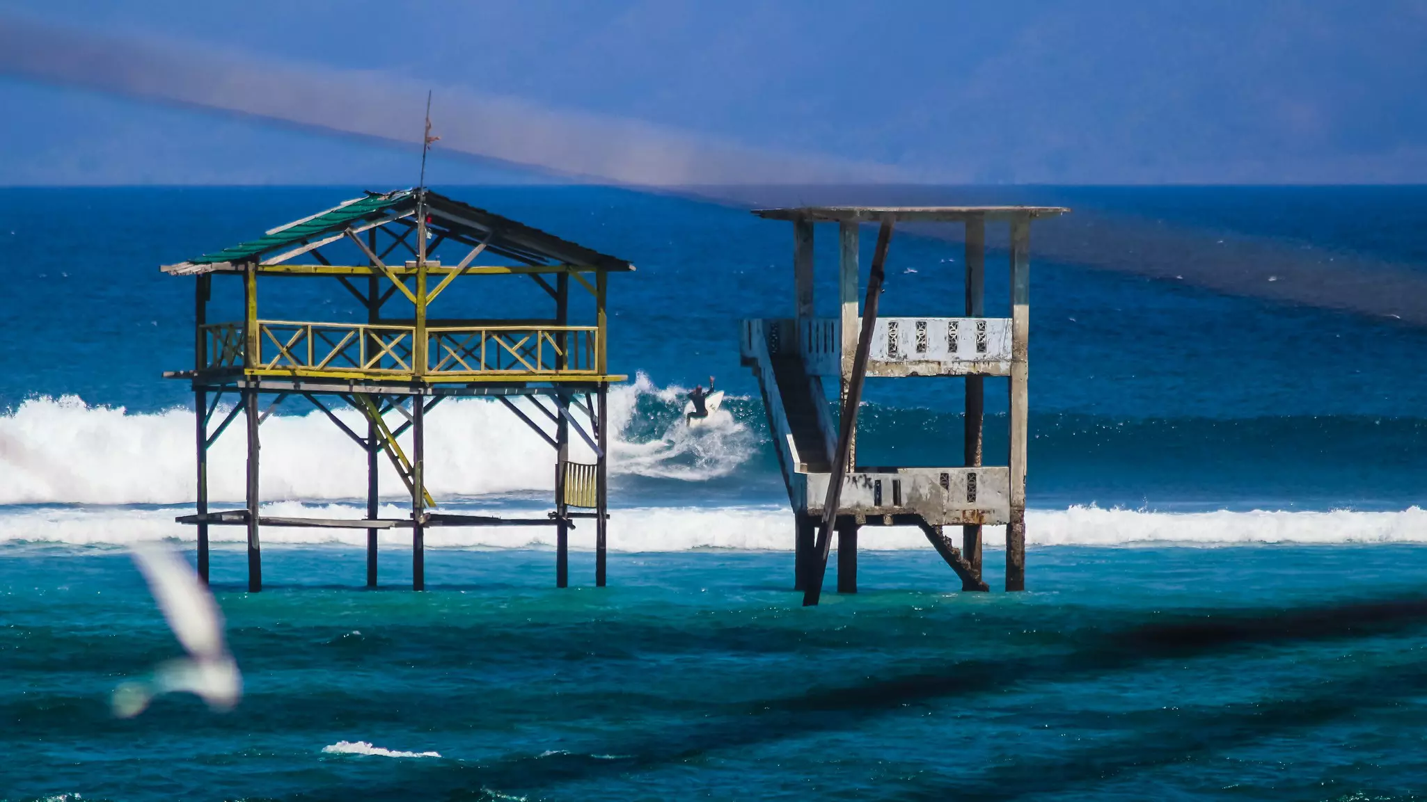 Two observation towers rise from the water near a large surfing break in a tropical locale.