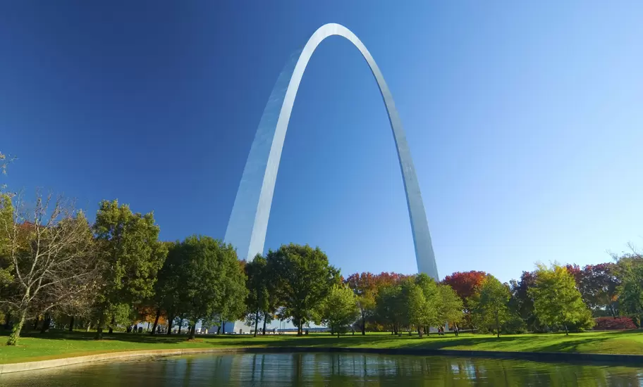View of the Gateway Arch, trees, and lake in the Jefferson National Expansion Memorial in St. Louis, Missouri on a sunny day.