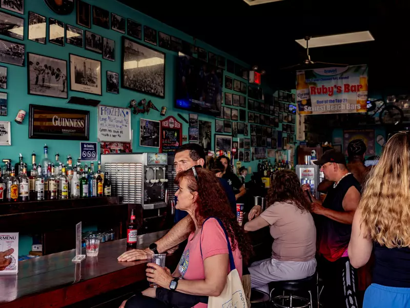 People sit at dark wood bar with bottles on the opposite shelf.
