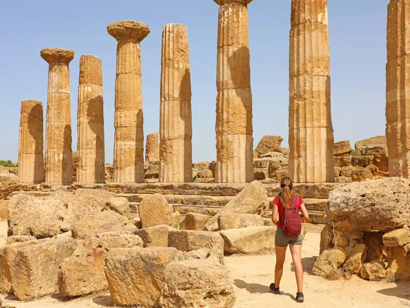 Young woman walking through the ancient columns in the Valley of the Temples in Agrigento.