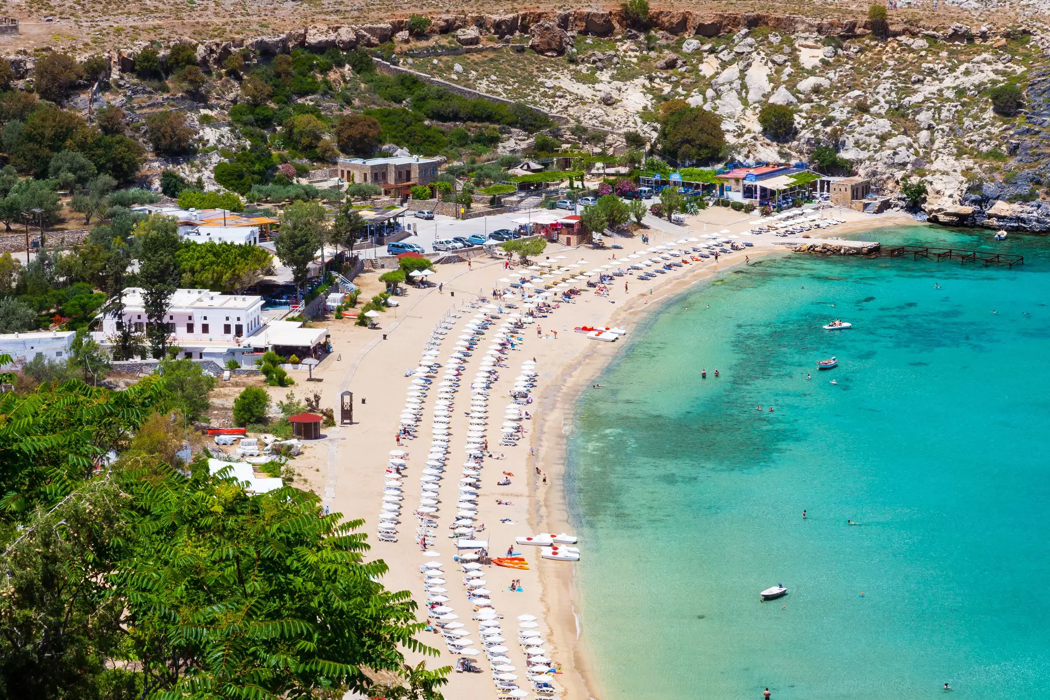 A crescent-shaped sandy beach full of sunbathers on a sunny day