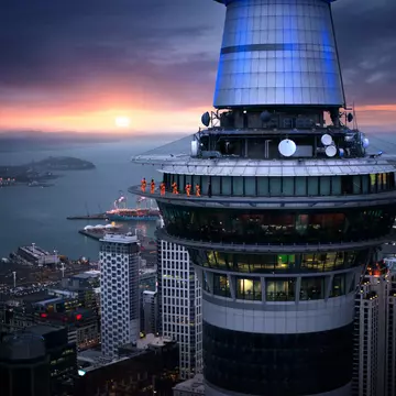 A group of thrill seekers in jumpsuits walk around the edge of the Sky Tower as the sun sets on the horizon in Auckland, New Zealand.