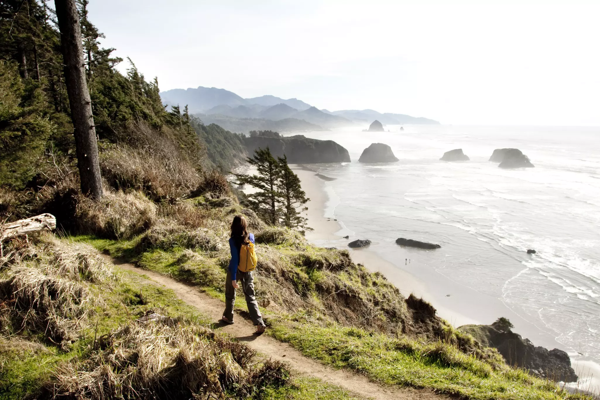 Female hiker walking along a secluded coastline path in Ecola State Park.