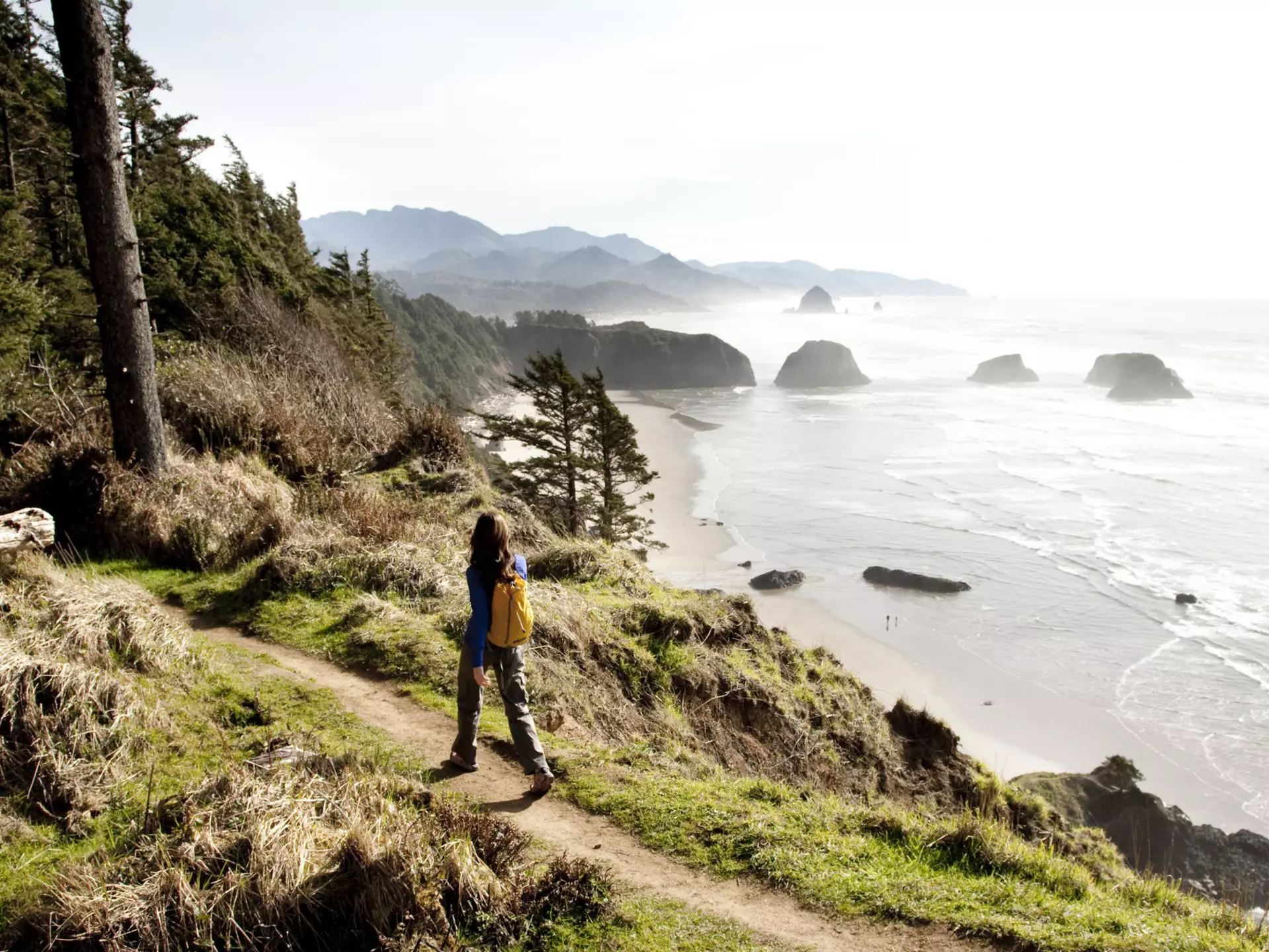 A woman hiking a secluded path along a rocky coastline.
