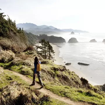 A woman hiking a secluded path along a rocky coastline.