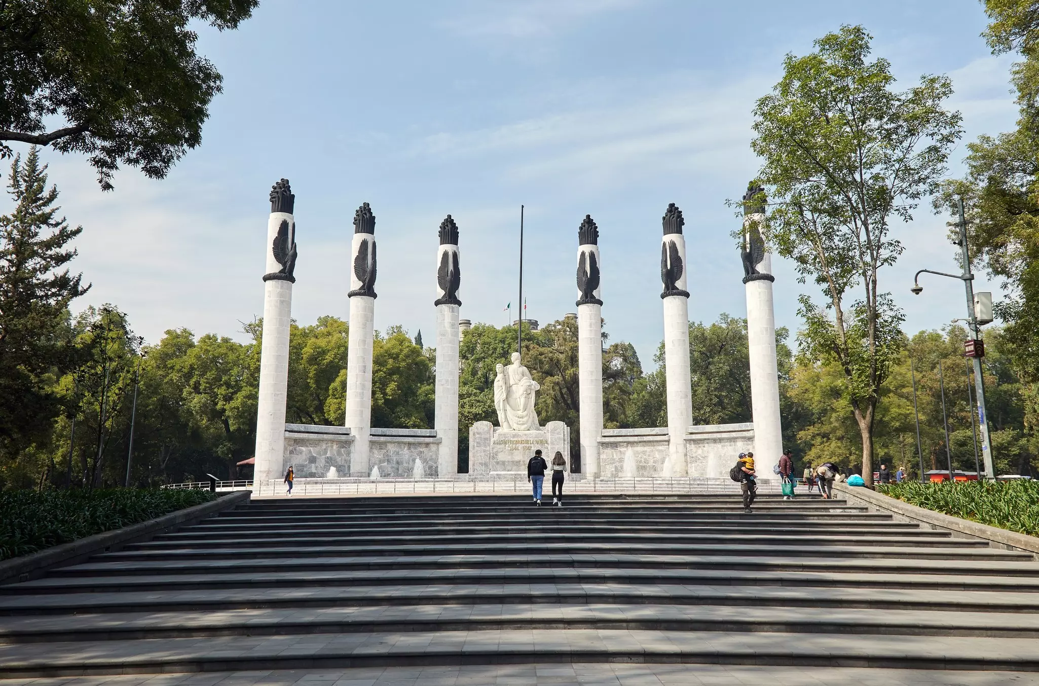 People walking on the stairs in front of the Monumento a los Niños Heroes, six pillars with a statue in the middle