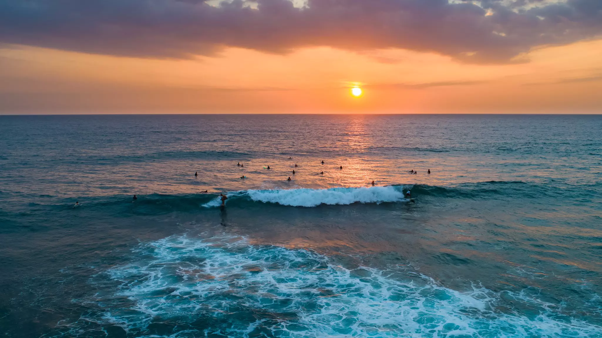 A group of surfers in the water at sunset.