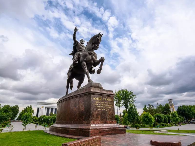 An equestrian sculpture of an emperor is on a plinth in a large city square.