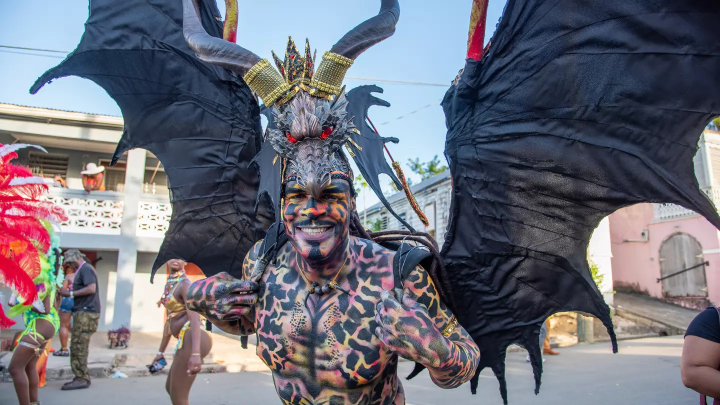 A man in a winged costume and covered in body paint smiles at the camera during Carnival in St Croix