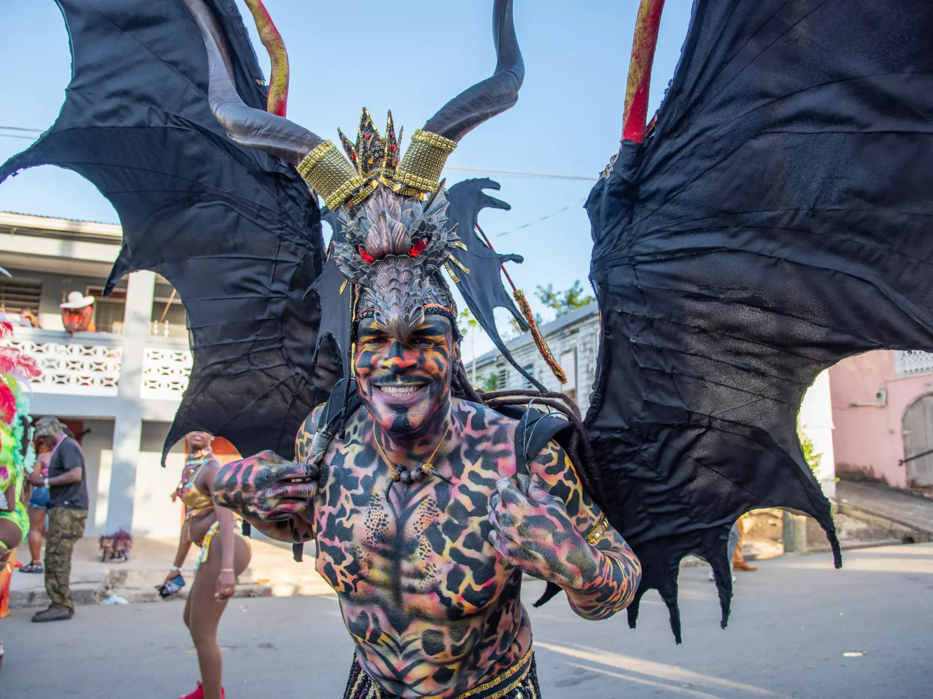 A man in a winged costume and covered in body paint smiles at the camera during Carnival in St Croix