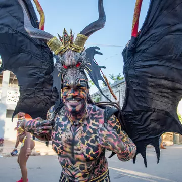 A man in a winged costume and covered in body paint smiles at the camera during Carnival in St Croix