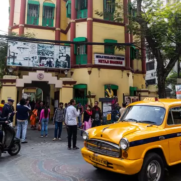 Exterior of Netaji Bhawan in Kolkata (Calcutta), West Bengal, India. People standing outside and yellow taxi driving past.