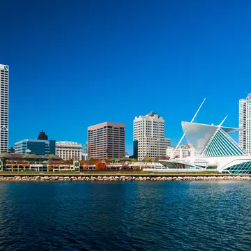 A lakefront city skyline with a modern art building to the right on a sunny day.