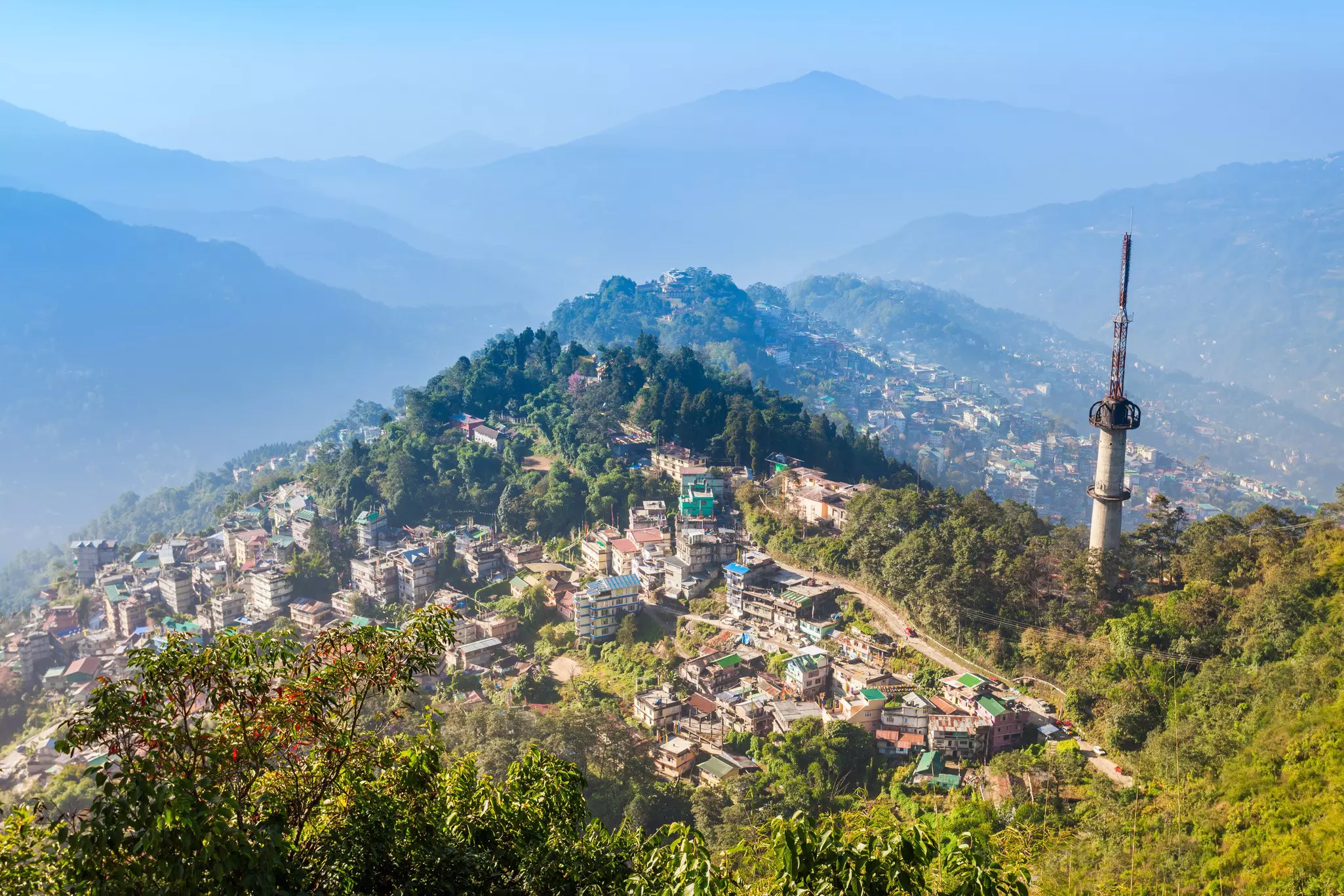 A small city spread out on hillsides and mountain peaks surrounded by green foliage