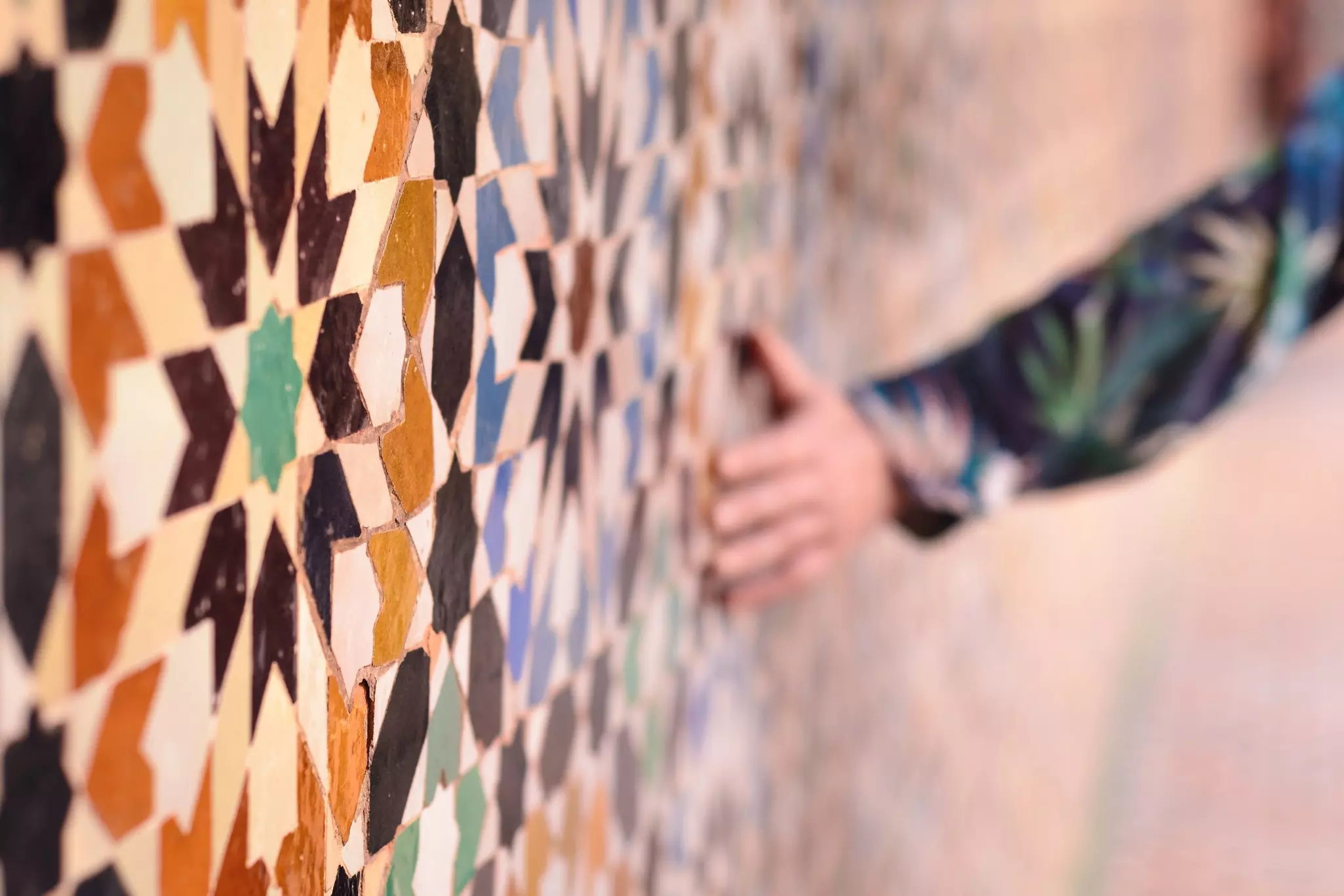 A hand touching tiles in a colorful geometric pattern.