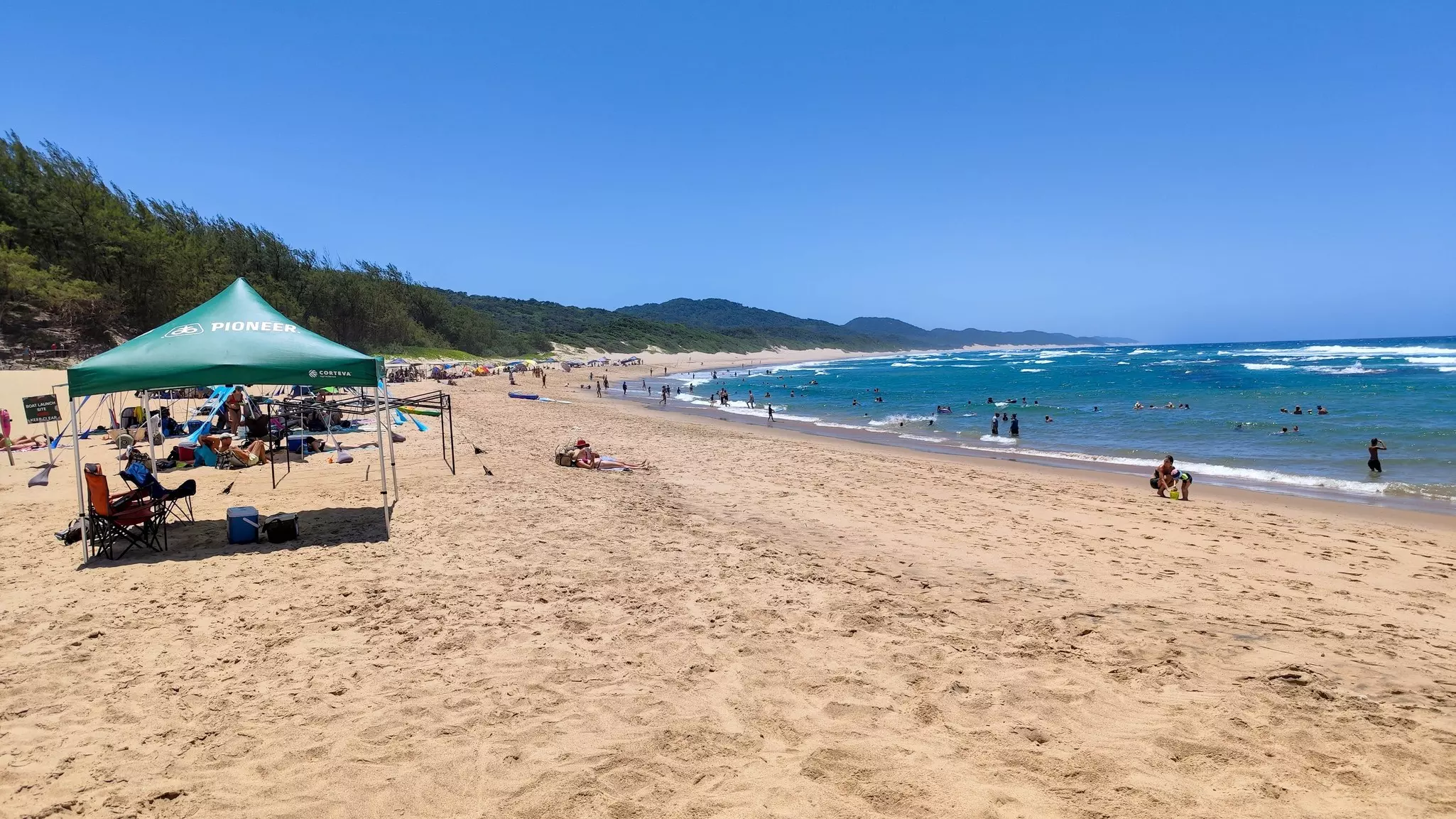 Families and groups set up for a day on the beach with sunshades and chairs.