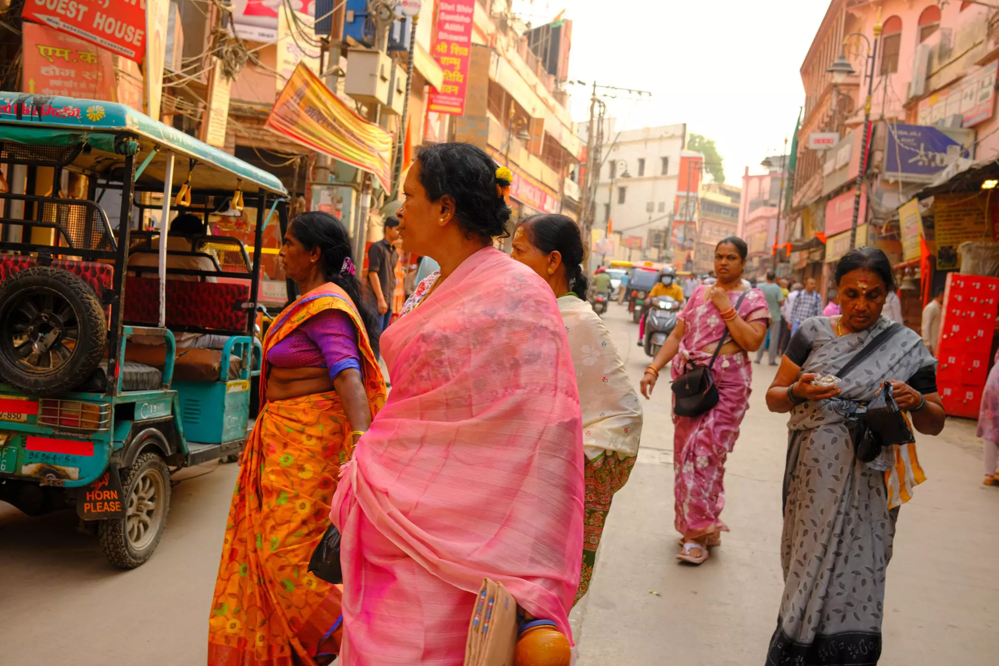 A group of women wearing colorful saris cross a city street.