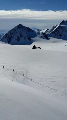 A woman in ski gear smiles for a phot in front of a snow-covered range of mountains.