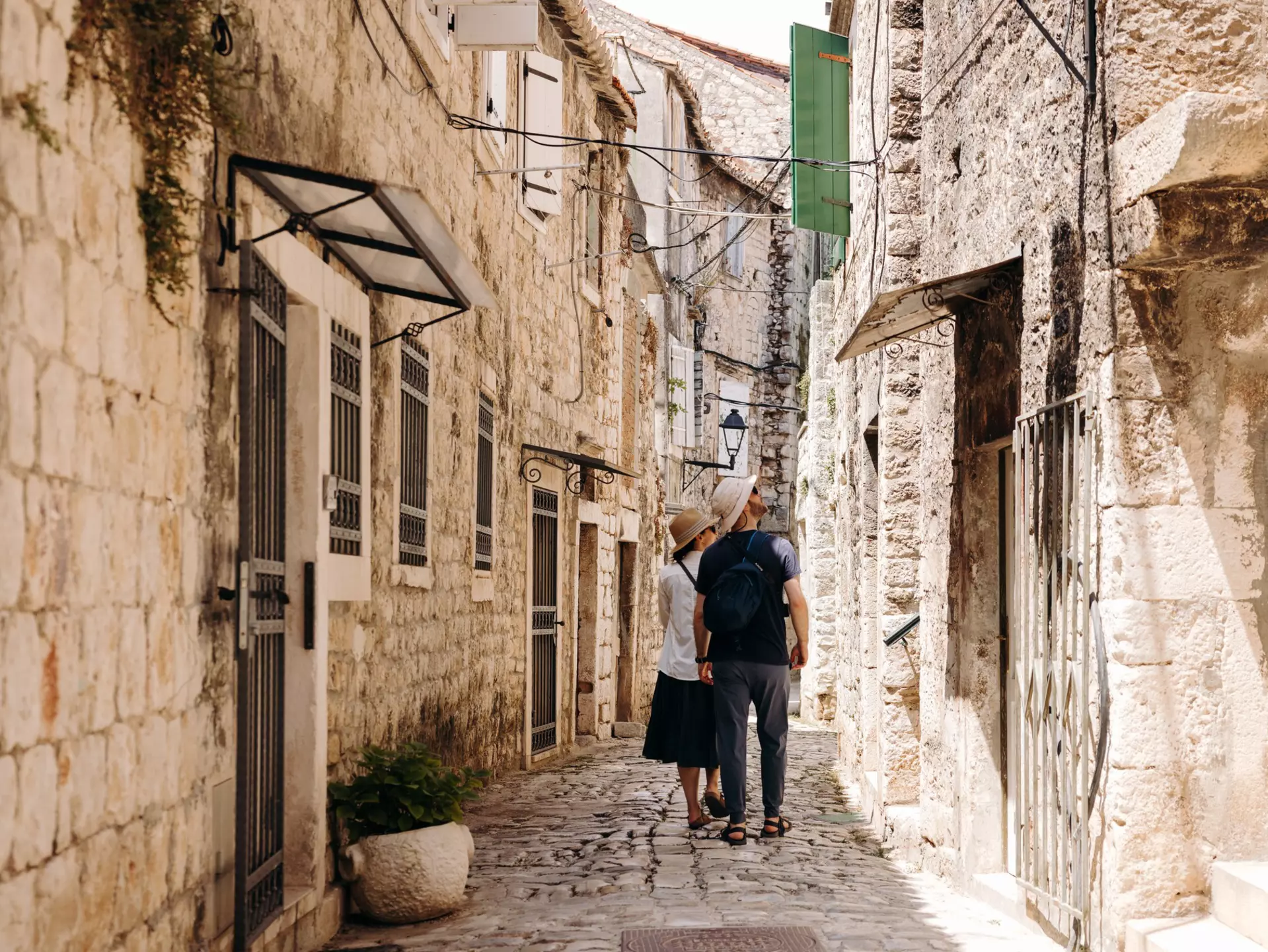 People walk on a narrow street looking up at the stone buildings.