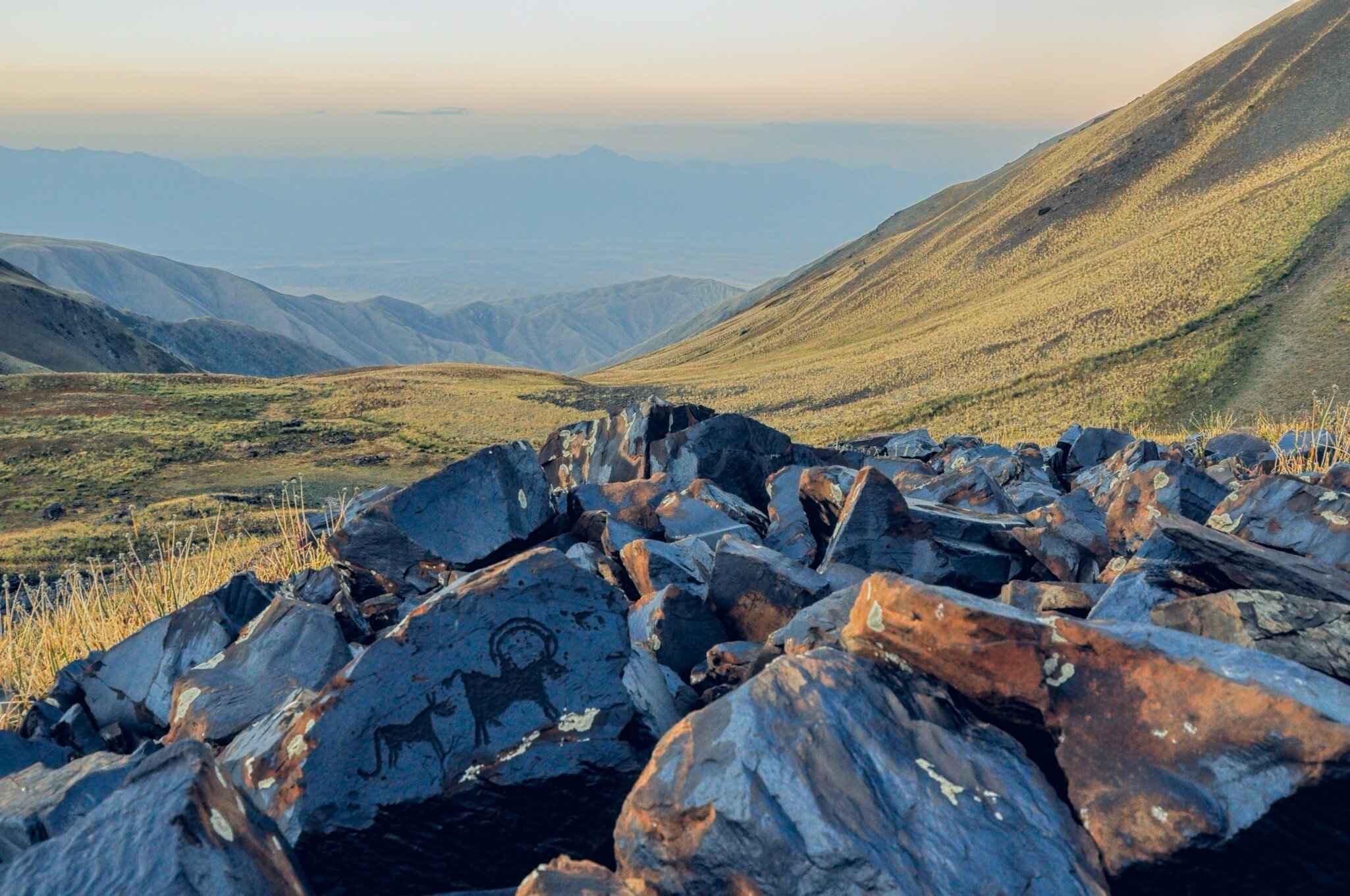 Rocks with pictograms in the foreground with sweeping, grass-covered hills and mountains stretching into the distance on a hazy day.