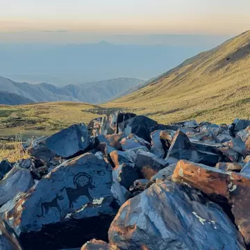 Rocks with pictograms in the foreground with sweeping, grass-covered hills and mountains stretching into the distance on a hazy day.