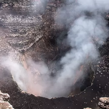 Looking down into a deep, layered volcanic pit with white gas drifting up from its floor