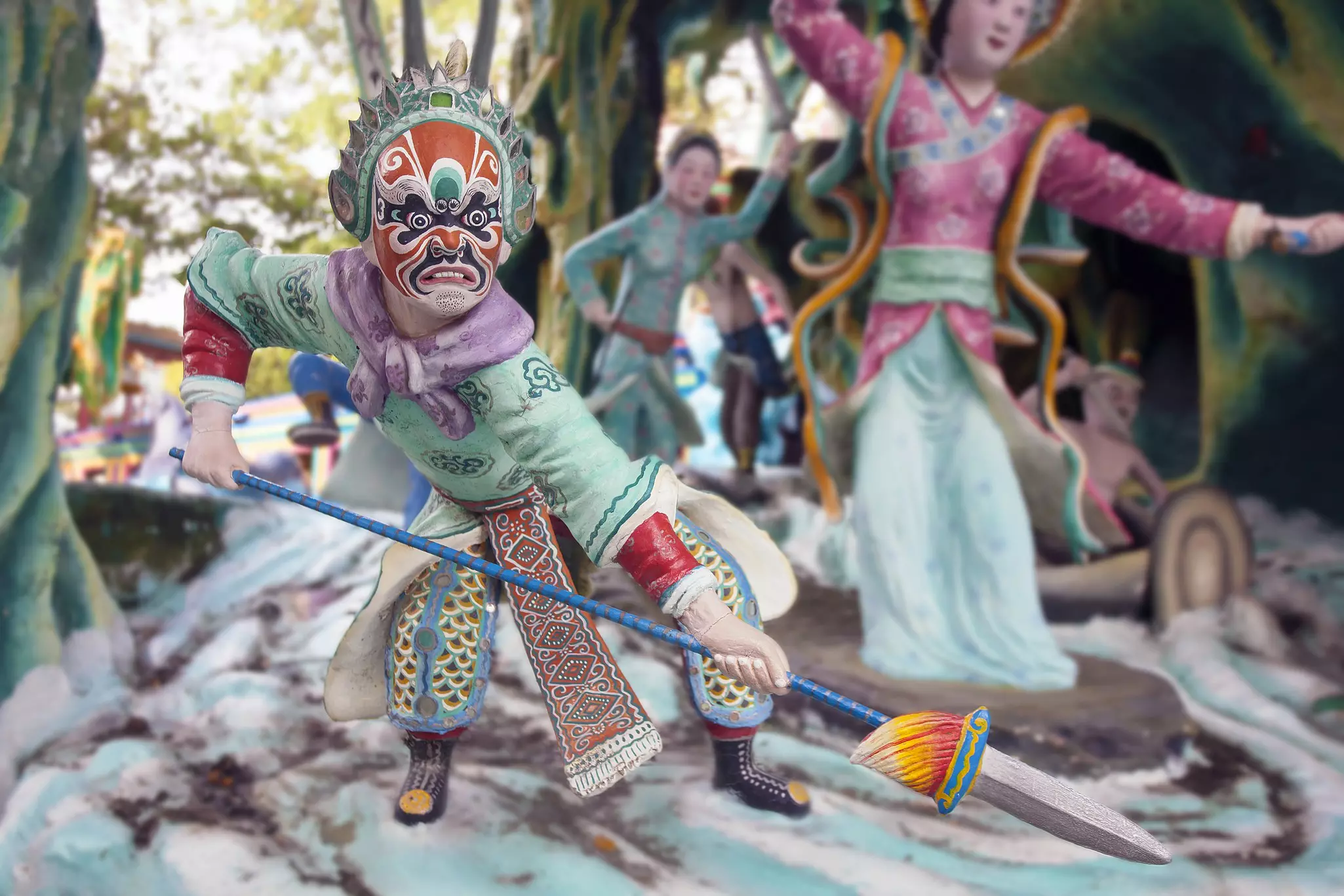 Figurines depicting a masked warrior and dancing woman are displayed in a park.