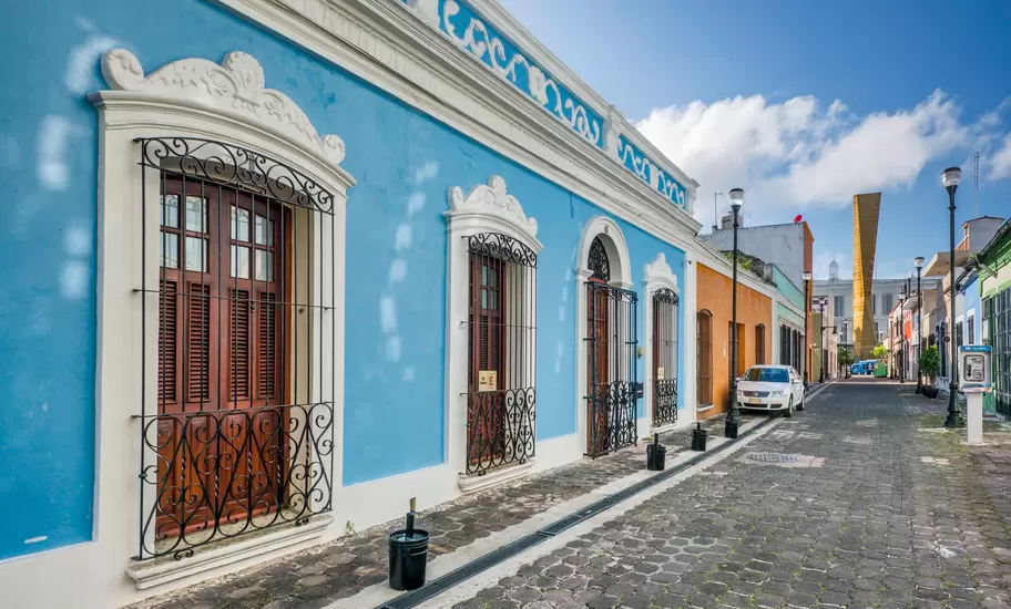 Blue colonial house with ornate white trim and iron window grilles on a cobbled street in Villahermosa, Tabasco
