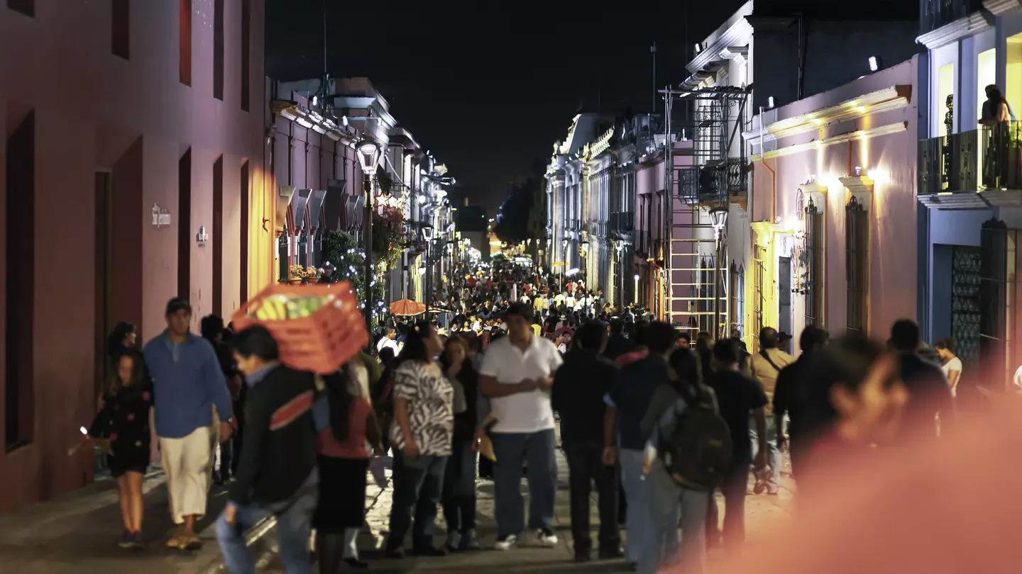 We see a crowded night street in downtown Oaxaca City in Mexico, during the celebration time and annual Guelaguetza celebration. the street is very crowded; the focus is in the background; the front people are in soft focus.