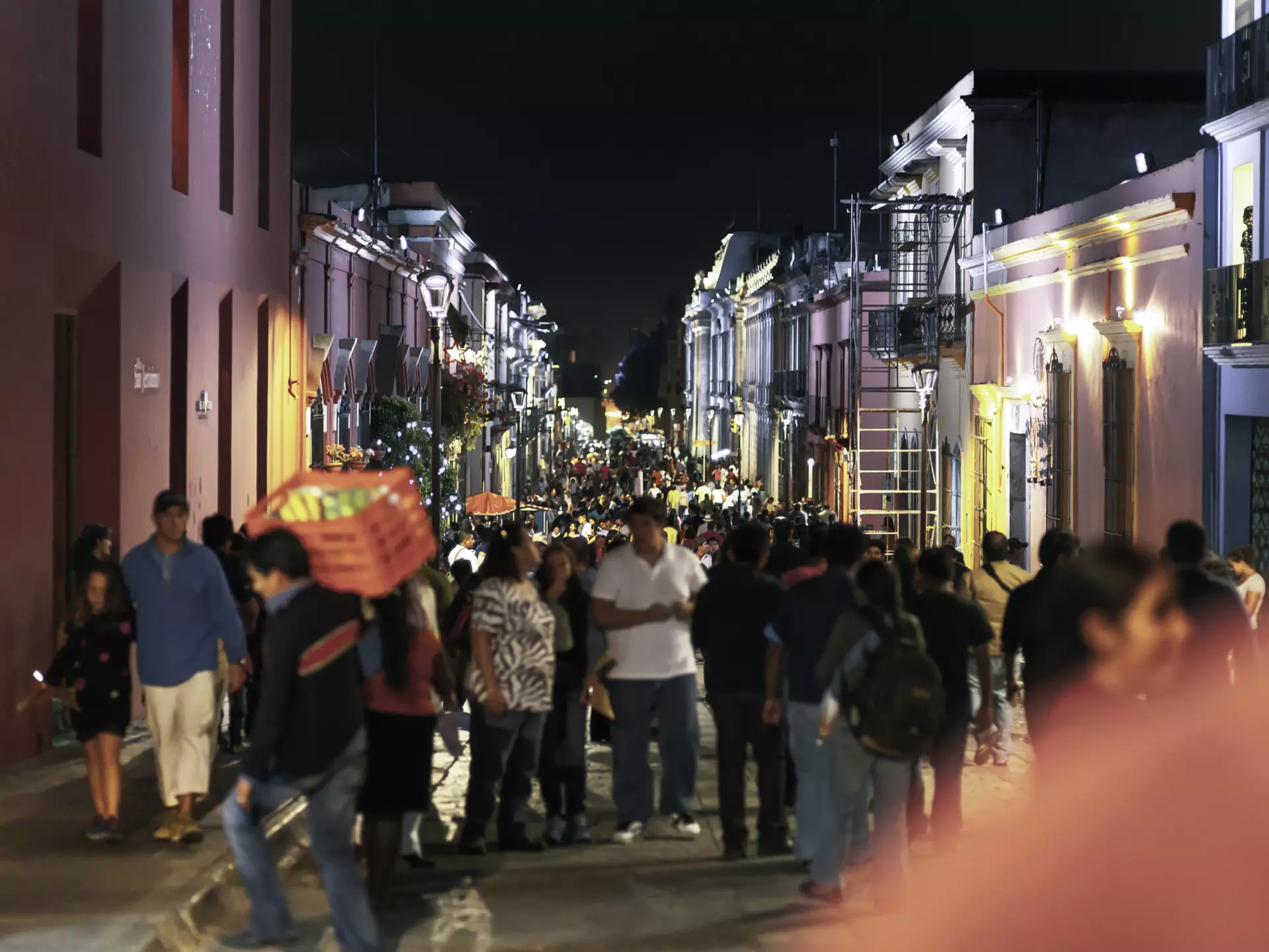 We see a crowded night street in downtown Oaxaca City in Mexico, during the celebration time and annual Guelaguetza celebration. the street is very crowded; the focus is in the background; the front people are in soft focus.