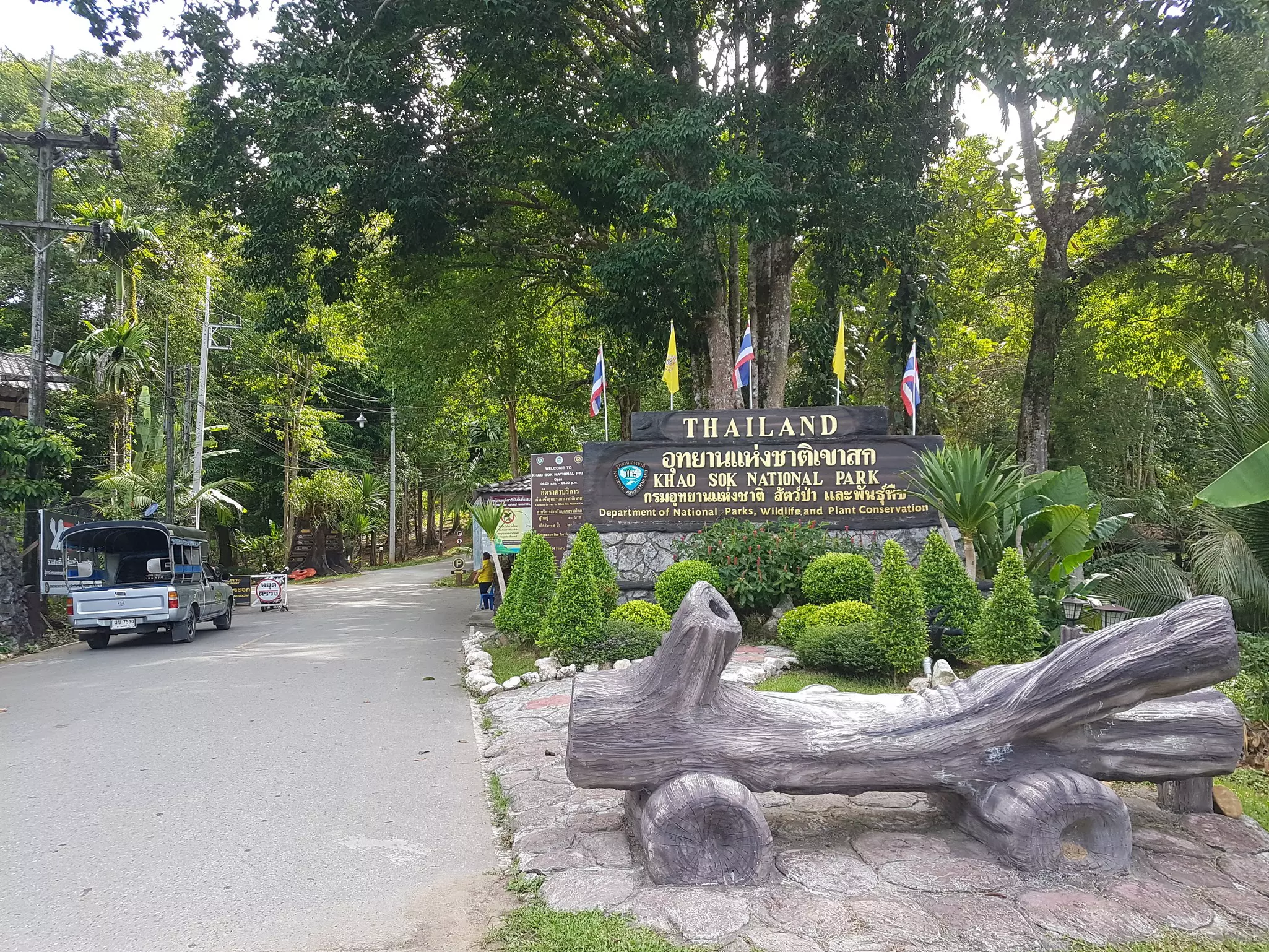 A park entrance with a wooden sign that says "Thailand" with words in Thai and "Khao Sok National Park."